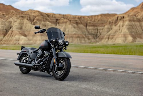 Harley-Davidson Deadwood – mattschwarzer Cruiser in Frontansicht schräg, geparkt auf einer Straße vor den Felsen der Badlands unter blauem Himmel