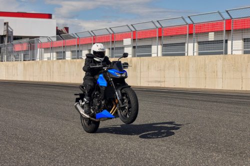 Honda CB750 Hornet 2027 in Glint Wave Blue auf der Start-Ziel-Geraden einer Rennstrecke, Frontansicht vor Betonmauer und Fangzaun