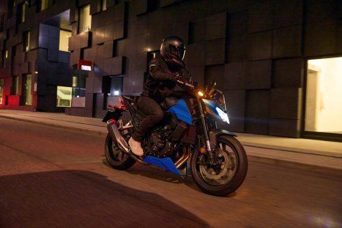 Honda CB750 Hornet 2027 in Glint Wave Blue bei Nacht in der Stadt, eingeschalteter LED-Doppelscheinwerfer, Seitenansicht von schräg vorn