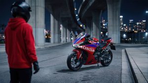 Fahrer in rotem Hoodie und Helm neben der Honda CBR500R FOUR 2027 in Ignition Red Tricolour nachts in der Stadt