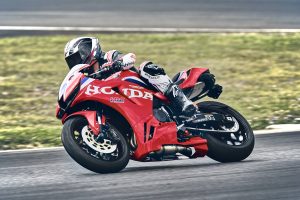 Honda CBR600RR 2027 in Ignition Red HRC TriColour in Schräglage auf der Rennstrecke, Fahrer mit Knie am Boden