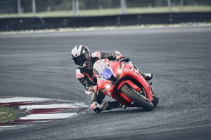 Honda CBR600RR 2027 in Ignition Red HRC TriColour in Schräglage am Kurvenscheitel, Frontansicht mit eingeschaltetem LED-Scheinwerfer