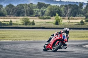 Honda CBR600RR 2027 in Ignition Red HRC TriColour in Schräglage vor Waldkulisse an der Rennstrecke