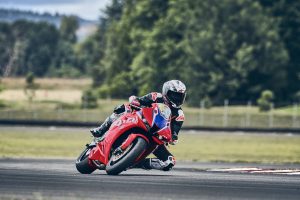 Honda CBR600RR 2027 in Ignition Red HRC TriColour in Rechtskurve vor Nadelbäumen
