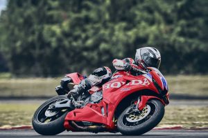 Honda CBR600RR 2027 in Ignition Red HRC TriColour in Schräglage nach links, Nahaufnahme von Fahrer und Verkleidung