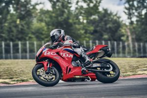 Honda CBR600RR 2027 in Ignition Red HRC TriColour in Linkskurve am Streckenrand mit Zaun