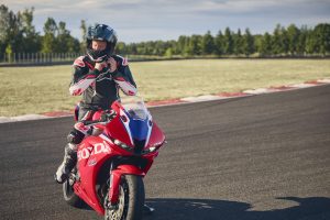 Fahrer schließt den Helm auf der Honda CBR600RR 2027 in Ignition Red HRC TriColour an der Rennstrecke