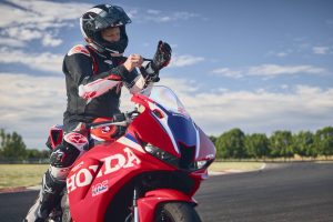 Fahrer zieht die Handschuhe an, sitzend auf der Honda CBR600RR 2027 in Ignition Red HRC TriColour