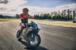 Fahrer in rotem Helm und Lederkombi auf der Honda CBR600RR 2027 in Matt Ballistic Black Metallic an der Rennstrecke