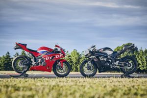 Honda CBR600RR 2027 in Ignition Red HRC TriColour und Matt Ballistic Black Metallic nebeneinander vor Bäumen, Seitenansicht