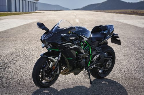 Kawasaki Ninja H2 2027 – Dreiviertelansicht von vorne links auf einem Flugfeld vor Hangar und Bergen
