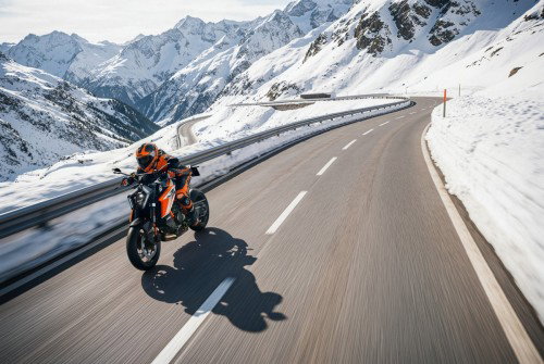 KTM 1390 Super Duke RR 2026 – Action-Aufnahme: Fahrer auf Alpenpassstraße mit Serpentinen und verschneiten Gipfeln