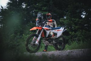 KTM 690 Rally 2027 – Fahrer in Enduro-Montur neben dem Motorrad auf einem Waldweg in der Dämmerung