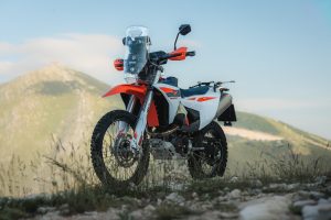 KTM 690 Rally 2027 – auf steinigem Untergrund vor Berglandschaft abgestellt, Ansicht von vorn links mit Rally-Tower