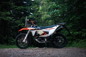 KTM 690 Rally 2027 – Seitenansicht von links auf Schotterweg im Wald, weiß-oranges Dekor mit Rally-Tower und Windschild