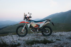 KTM 690 Rally 2027 – Seitenansicht von links auf hellem Geröll vor Bergpanorama in der Dämmerung, Rally-Tower und Auspuff sichtbar
