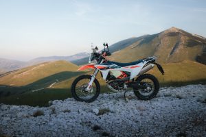 KTM 690 Rally 2027 – Seitenansicht von rechts auf einem Geröllfeld vor sonnenbeschienenen Berggipfeln