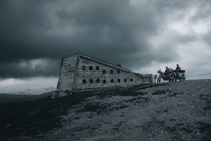 KTM 690 Rally 2027 – zwei Fahrer mit bepackten Maschinen an einer Bergruine unter dunkler Wolkendecke