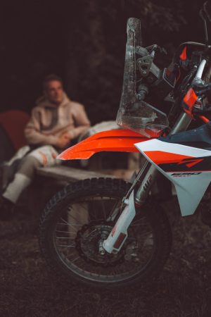 KTM 690 Rally 2027 – Frontpartie mit Windschild und Kotflügel im Vordergrund, im Hintergrund ein sitzender Fahrer am Lagerplatz
