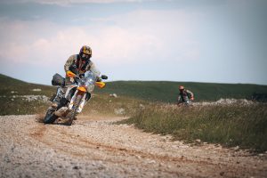 KTM 690 Rally 2027 – Frontansicht in Schräglage auf heller Schotterpiste, zweiter Fahrer folgt im Hintergrund