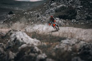 KTM 690 Rally 2027 – Fahrer driftet mit Staubfahne über steinige Schotterpiste in karger Felslandschaft