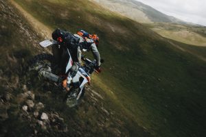 KTM 690 Rally 2027 – Aufnahme von oben auf den stehend fahrenden Fahrer beim Bergabritt über einen steilen Grashang