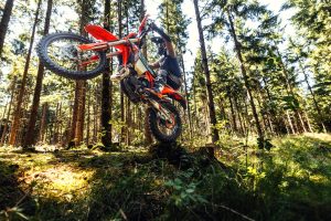 KTM 300 EXC 6DAYS 2027 – Fahrer springt mit dem Zweitakt-Enduro über einen Geländesprung im lichten Nadelwald