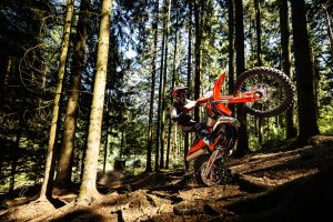 KTM 300 EXC 6DAYS 2027 – Fahrer klettert mit angehobenem Vorderrad eine Waldstufe hinauf