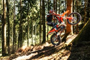 KTM 300 EXC 6DAYS 2027 – Zweitakt-Enduro springt in einer Staubwolke einen Waldabhang hinab