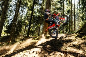 KTM 300 EXC 6DAYS 2027 – Fahrer mit angehobenem Vorderrad auf sonnigem Hang mit aufgewirbeltem Staub