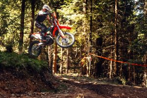 KTM 450 EXC-F 6DAYS 2027 – Fahrer springt auf einem abgesperrten Waldtrail über eine Kuppe