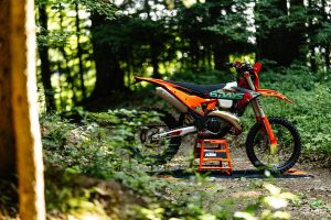 KTM 300 EXC 6DAYS 2027 – Seitenansicht auf orangefarbenem Paddock-Ständer im Wald