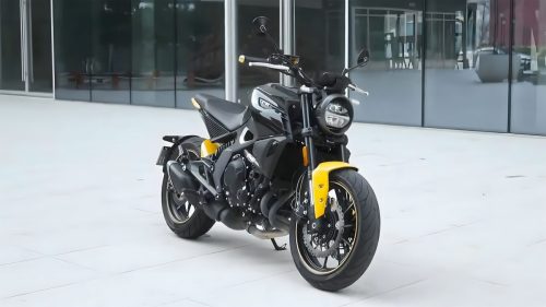 Letbe Arthur 700 2026 – Naked Bike in Schwarz-Gelb, Dreiviertelansicht von rechts vorne vor modernem Glasgebaeude, gelber Kotfluegel sichtbar
