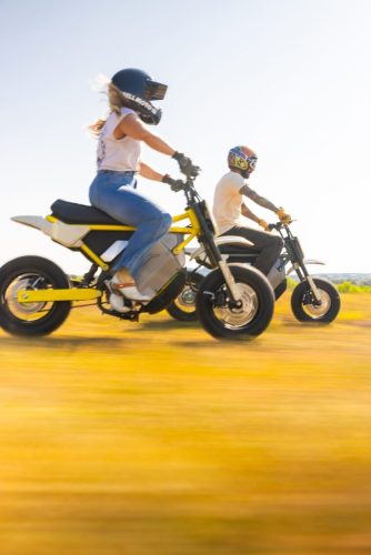 LiveWire S4 Honcho 2026 – zwei Fahrer auf dem gelben und dem grauen Minibike bei der Fahrt durch ein goldenes Feld, Bewegungsunschärfe