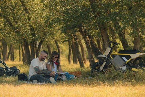 LiveWire S4 Honcho 2026 – Paar sitzt zum Picknick im Gras, das gelbe und das graue Minibike im Hintergrund abgestellt