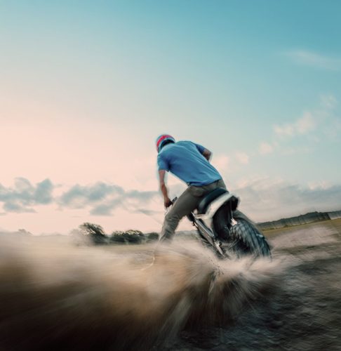 LiveWire S4 Honcho Trail 2026 in Weiß-Grau – Fahrer driftet über losen Untergrund und wirft eine Staubfahne auf, Heckansicht