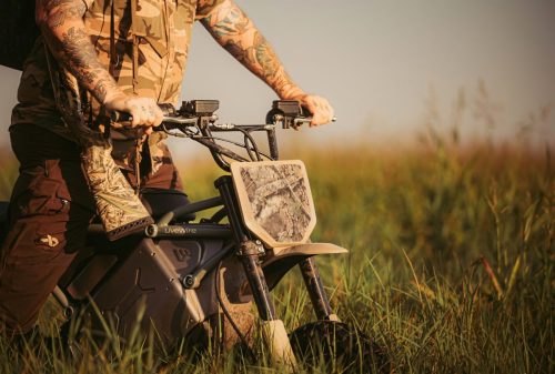 LiveWire S4 Honcho Trail 2026 – Detail des Lenkers mit Tarnmuster-Nummernschild, Fahrer in Camo im hohen Gras