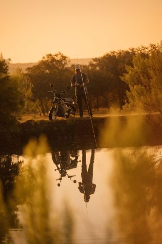 LiveWire S4 Honcho Street 2026 in Gelb – Weitwinkel: Mann angelt am See, das Minibike daneben abgestellt, mit Spiegelung im Wasser
