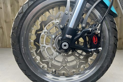 Mac Motorcycles Rex Ruby 2026 – Vorderrad mit 17-Zoll-Speichenfelge, 320mm-Schwimmscheibe und HEL-Bremssattel an Fastace-USD-Gabel im Werkstatt-Setting