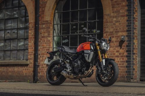 Suzuki GSX-8T 2027 in Glass Blaze Orange mit goldener Upside-down-Gabel, Dreiviertelansicht vor einer Backsteinhalle