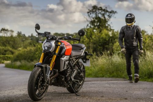 Suzuki GSX-8T 2027 in Glass Blaze Orange am Straßenrand, Fahrer in Lederkombi läuft auf das Motorrad zu