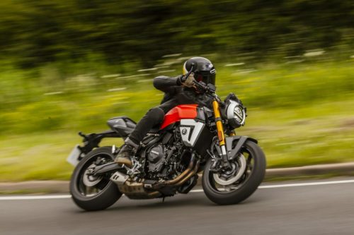 Suzuki GSX-8T 2027 in Glass Blaze Orange in Fahrt auf einer Landstraße, Mitzieher mit grünem Hintergrund