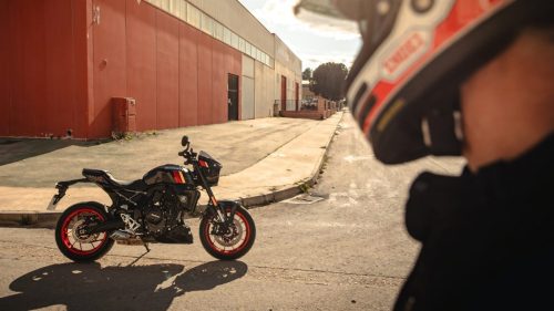 Suzuki GSX-8TT in Schwarz mit roten Felgenrändern auf einem Industriegelände, im Vordergrund Fahrer mit Helm