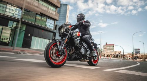Suzuki GSX-8TT in Schwarz mit roten Felgenrändern in Fahrt durch eine Stadtstraße mit moderner Architektur