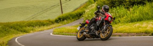 Suzuki GSX-8TT in Rot-Gold in Schräglage auf einer kurvigen Landstraße, Panoramaformat