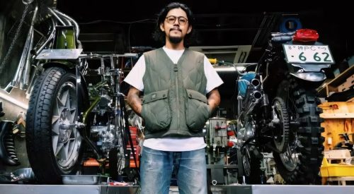 Custom-Bike-Builder Satoshi in grüner Steppweste zwischen zwei Motorrad-Umbauten in seiner Werkstatt in Japan