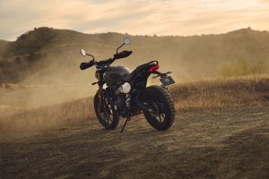 Triumph Scrambler 400 X 2027 – Dreiviertel-Heckansicht auf staubigem Gelände im Abendlicht