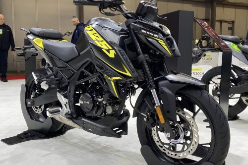 Voge R125S 2026 – Dreiviertelansicht vorne rechts in Schwarz Matt mit gelben Akzenten auf Messestand, Modellbezeichnungen KEL800 und B300H im Hintergrund