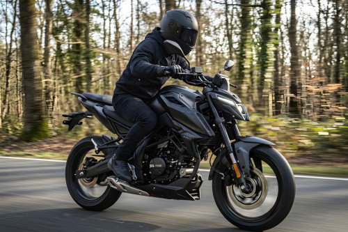 Voge R125S 2026 – Actionfoto in Fahrt auf Waldstraße, Dreiviertelansicht rechts, Fahrer in schwarzer Kleidung mit Helm, Bäume im unscharfen Hintergrund