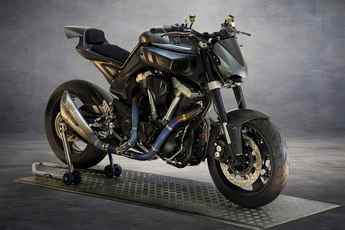 Yamaha MT-01 ORCO – Dreiviertelansicht von vorne rechts auf Metallgitter, dunkle Karbonfaser-Karosserie mit skulpturalem Intradosso-Design, V-Twin-Motor sichtbar